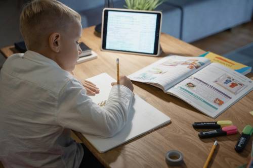 A student at a wooden desk using a laptop and taking notes, symbolising dissertation assistance by Scora for overwhelmed students.