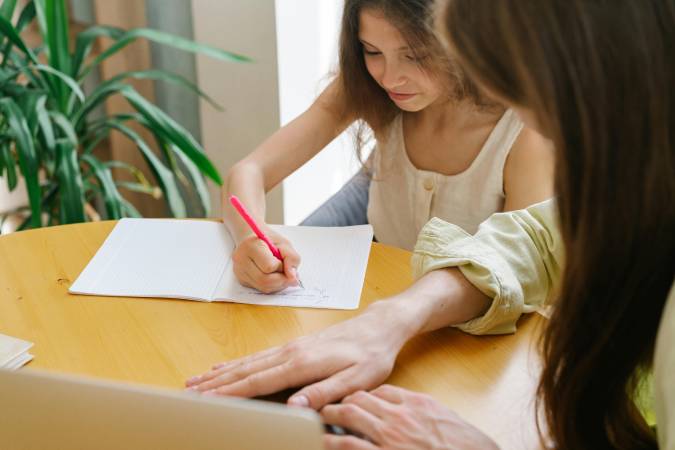 A student at a wooden desk using a laptop and taking notes, symbolising dissertation assistance by Scora for overwhelmed students.